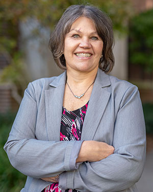 Brenda Kulhanek wears a gray blazer and print blouse and stands outside VUSN's building on a fall day