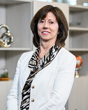 Patty Sengstack wearing a white jacked and print blouse leans against a desk