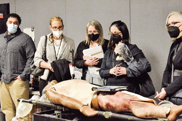 4 people in civilian clothes and wearing face masks look at a simulation mannequin at Blanchfield Army Community Hospital