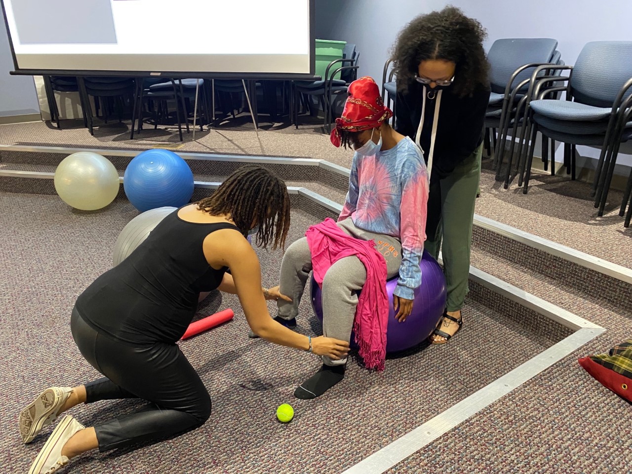 three people, one kneeling, one sitting on a ball and the other standing