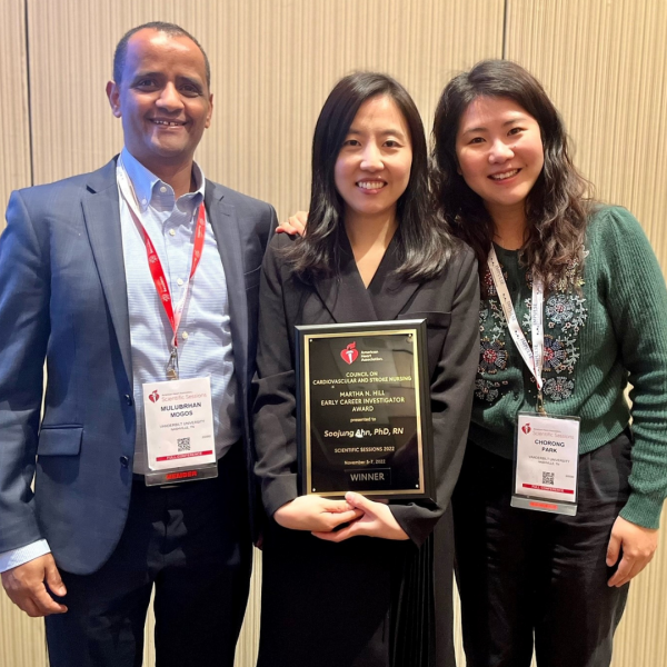 three people stand, smiling with an award