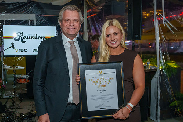 Vanderbilt Chancellor Daniel Diermeier in a suit with alumna Erin Miller holding a framed award