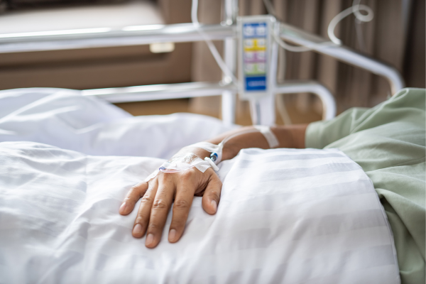 person laying in hospital bed, hand only showing, with IV