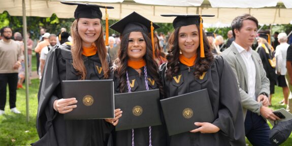 Three women in graduation robes holding their diplomas.