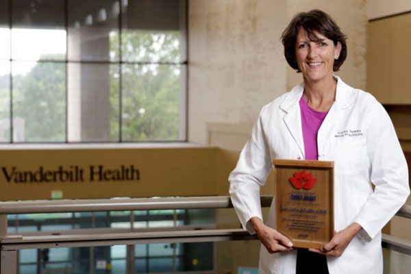 Tracey DeWire in white coat holds plaque award in front of Vanderbilt Health sign