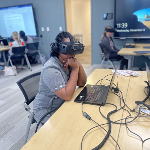 A woman sitting at a desk with a computer in front of her wearing a VR headset.