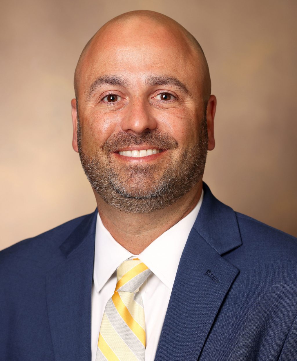 Man in blue suit and yellow tie smiles in headshot