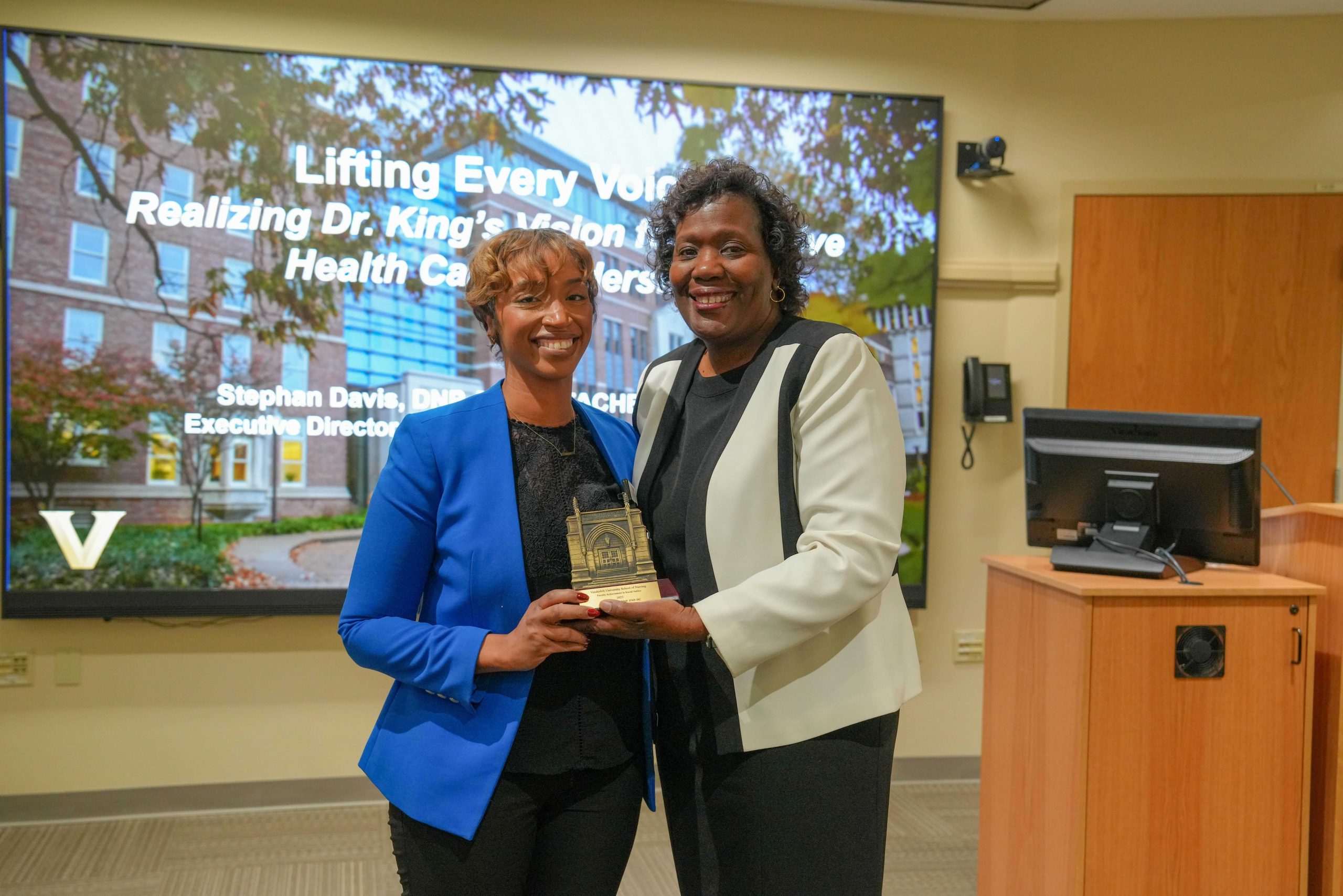 Two women holding an award in front of an overhead projecter.