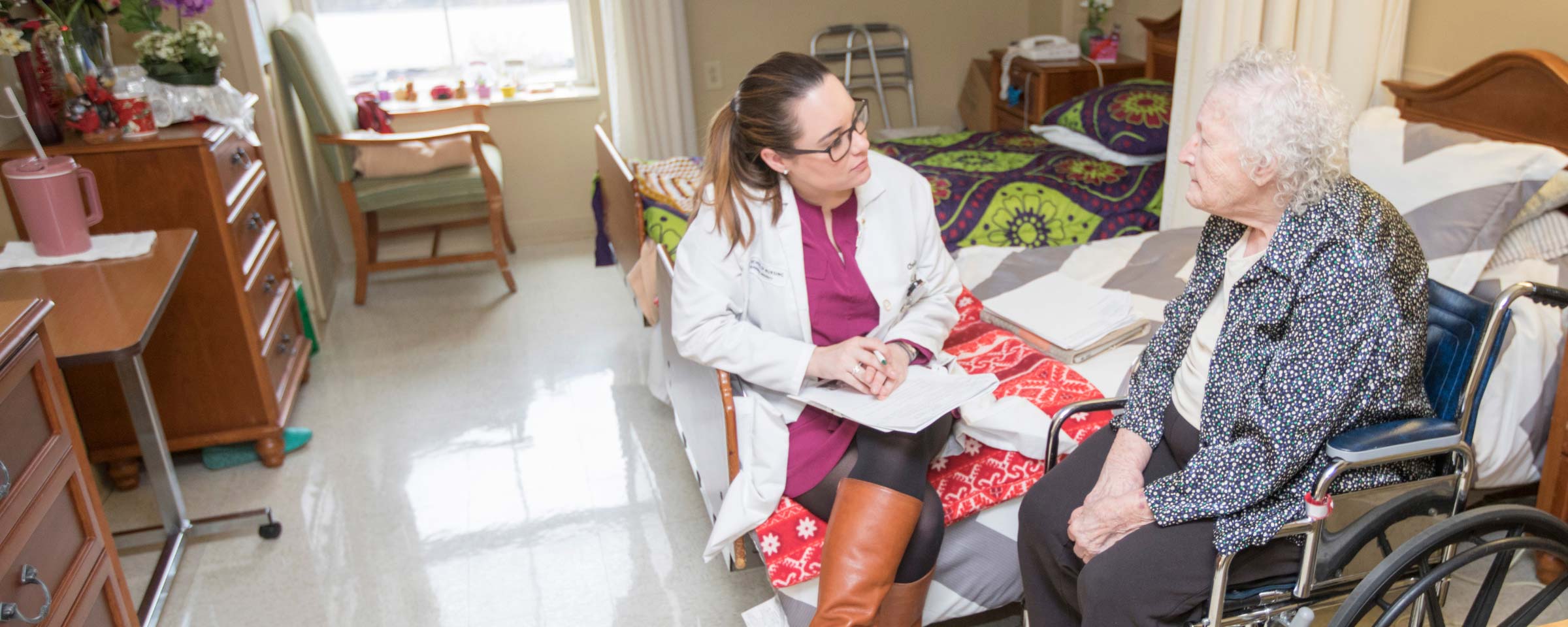 a nurse speaking with an elderly female patient in a wheelchair