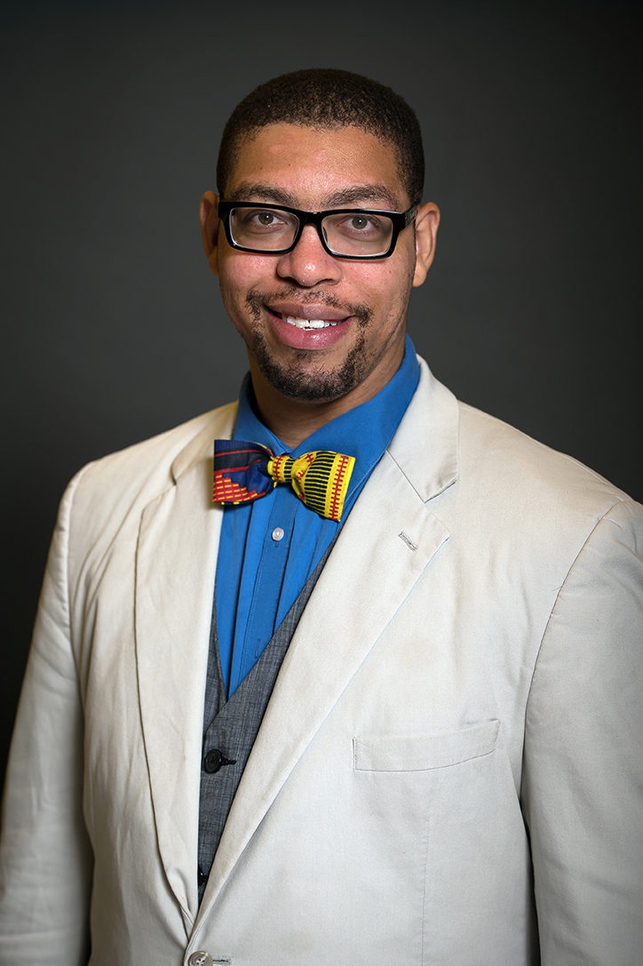 Portrait photo of Antentor Hinton, Jr. wearing glasses, a blue shirt, multi-colored bow tie, and a white coat.