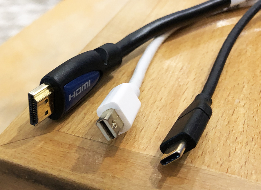 The tips of 3 cords sitting on a wooden surface: HDMI (left), Mini DisplayPort (middle), and USB-C (right).