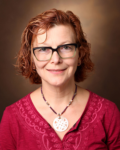 Headshot of Irina Kaverina wearing eye-glasses, a red top, and necklace with a round medallion. 