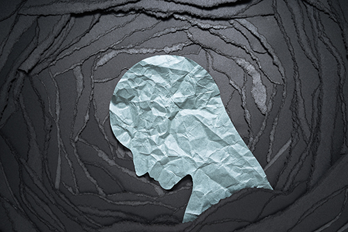 A teal piece of paper in the shape of a downcast head sits on top of torn black paper. The torn paper is arranged in concentric circles with the head in the center.