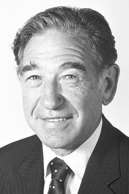 Black and white headshot of Stanley Cohen wearing a pin-stripe suit and dark tie with white diamonds.