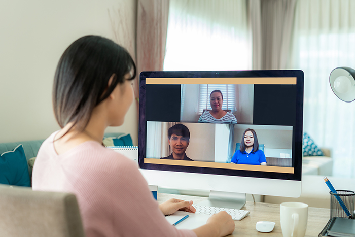 A person sitting at a desk is using a laptop to speak with three other people via a video conference.