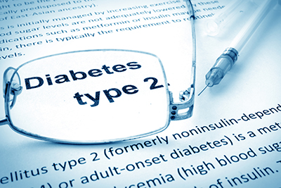 A close-up of a printed page that describes type 2 diabetes. A pair of reading glasses sitting on the page are magnifying the text, “Diabetes type 2."