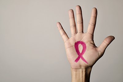 A human hand, palm open to the viewer, with a pink ribbon drawn on it. The pink ribbon is the chosen symbol for breast cancer awareness.