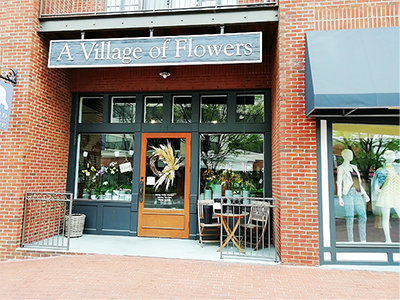 The storefront of a flower shop called “A Village of Flowers” with a “Closed” sign on its window.