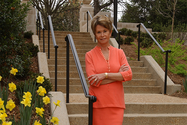 Colleen Conway-Welch in apricot colored suit stands on stone steps