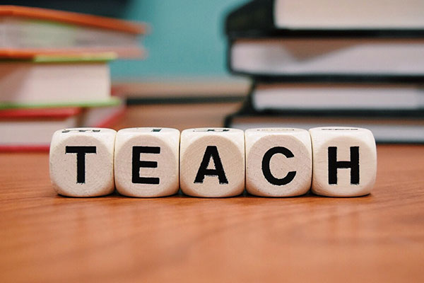 White dice spellling out teach in front of books