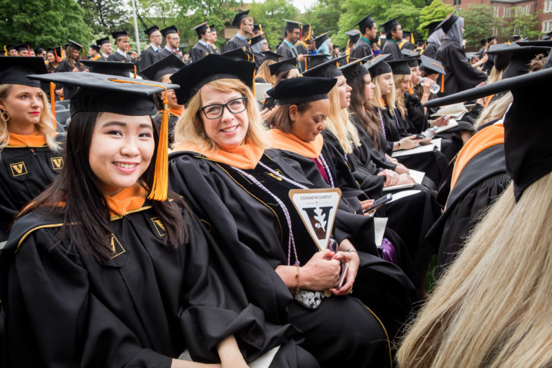 Rows of Vanderbilt graduates in gold and black robes sit waiting for Commencement to start. One is a master's graduate and the other is a doctor of nursing practice graduate.