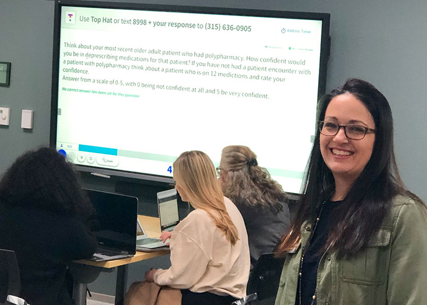 Instructor Kanah Lewallen stands in front of a large visual display that a group of students behind her are using to take a test.