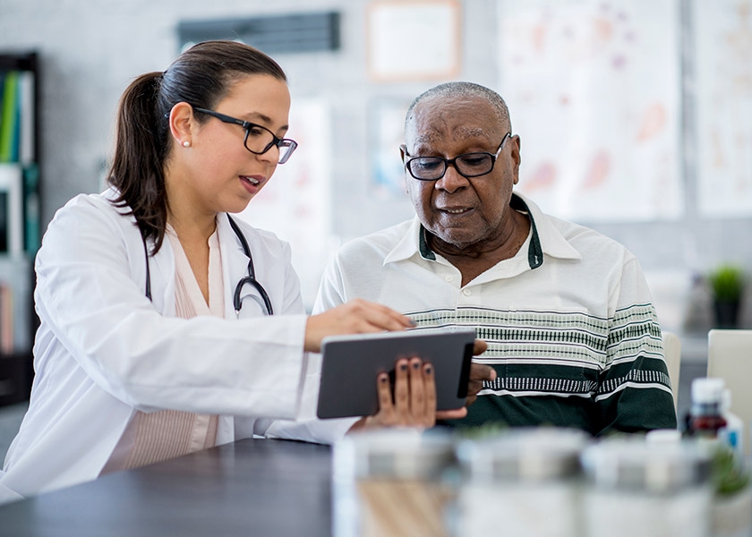 A female nurse practitioner shows something on a tablet to an older African American man