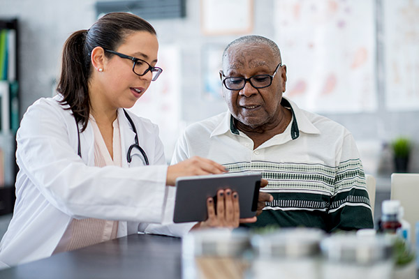 White female nurse practitioner shows something on a tablet to an older African American male patient