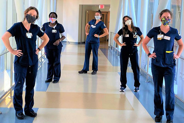 5 Nursing students in blue scrubs model colorful handmade cloth masks provided for them by alumni