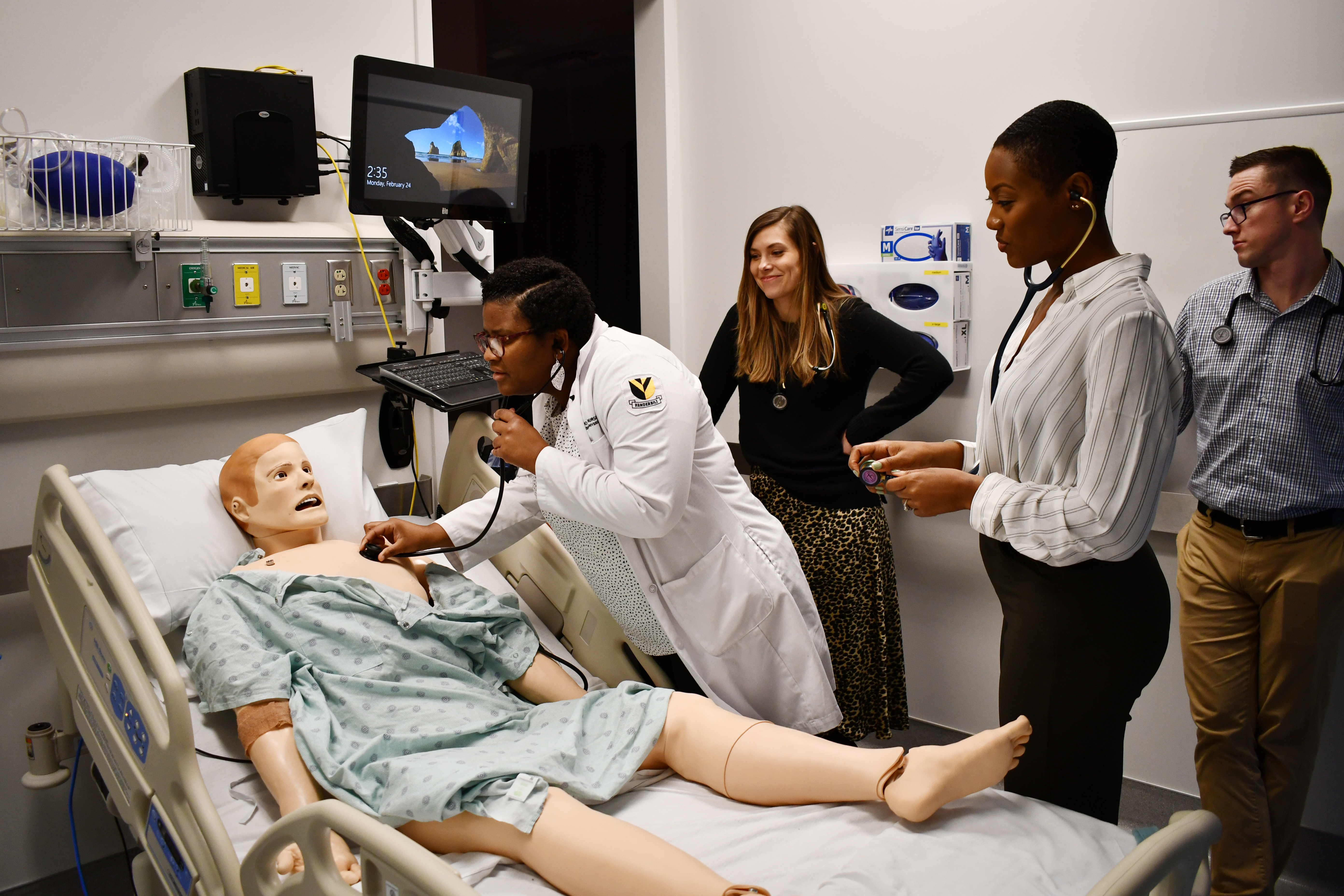 Nursing student examines mannequin in simulation lab while three other students look on