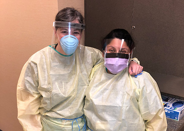 Nurse practitioners gowned and wearing face masks under clear shields 