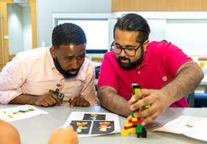 Two male students assemble a Lego figure.