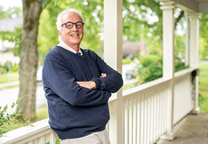 Professor Tom Christenbery leans against a white porch railing