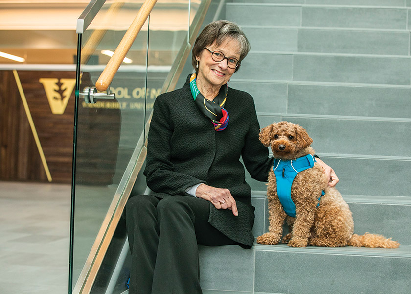 Professor Mary Jo Gilmer sits on steps in VUSN atrium. Her therapy colleague, a goldendoodle, sits next to her.
