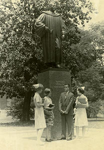 Old black and white photo of three female nursing students standing with a male student under the statue of Harold Vanderbilt