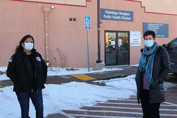 VUSN alumna Annie Moon and VUSM alumna Dr. Jill Moses in front of the health care center in Chinle, AZ, where they work. Both wear winter coats and face masks.