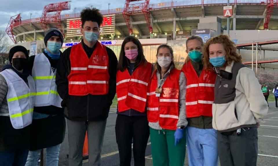 Seven people in safety vests and masks pose with professor Jennifer Wilbeck in front of Nissan Stadium