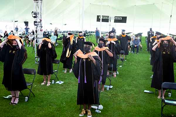 Group of graduates in academic regalia donning academic hoods