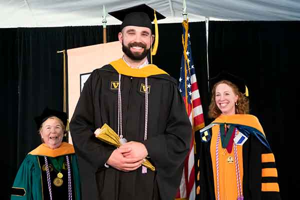 Dean Norman, MSN graduate William McConnell, Jennifer Wilbeck pose for a photo in front of the VUSN banner