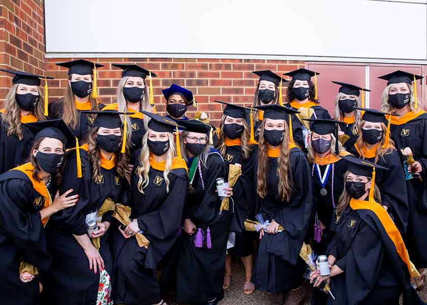 Nurse-Midwifery graduates and faculty pose after Commencement ceremonies. All are in academic robes and black masks.