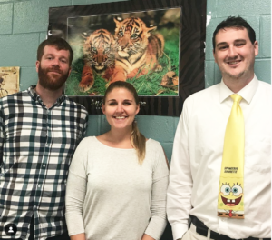 Biological Sciences lecturers Thomas Clements, Jessica Gilpin, and James Pask standing in front of a poster of tigers