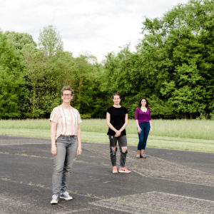 Photo of Jana Harper, Rebecca Steinberg, and Moksha Sommer standing in a parking lot with grass and trees in background