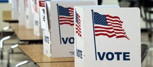 temporary cardboard voting booths decorated with the American flag and the word "VOTE" sit on desks in a voting precinct