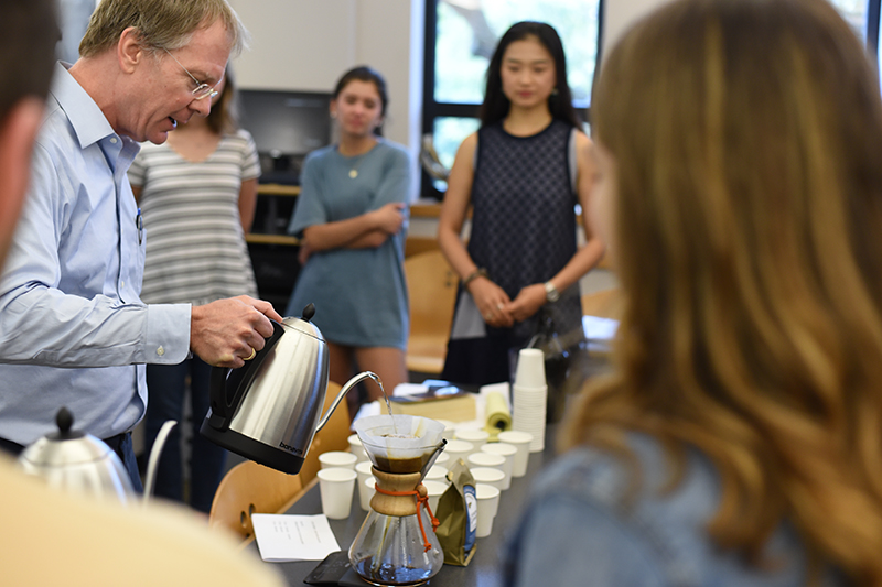 Ted Fischer pours water into a pourover coffee brewer as students watch