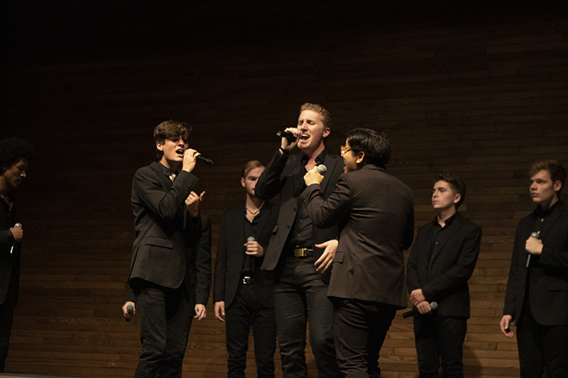 William Schmid and other Melodores stand on stage holding microphones and singing