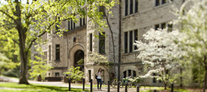 Exterior of Furman Hall, a gray stone building on the Vanderbilt campus, with blooming trees and a student walking by in the foreground