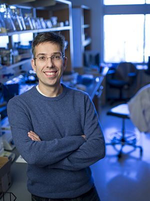 Antonis Rokas standing in his lab with a chair, lab coat, lab desk, and equipment behind him