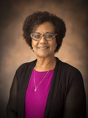 Associate Professor of African American and Diaspora Studies Tiffany Patterson wearing a pink blouse and black sweater and standing in front of a brown background