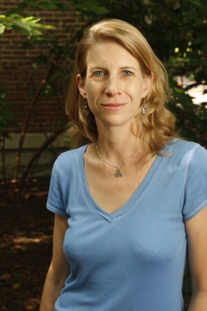 Laura Carpenter, wearing a blue shirt, stands in front of a tree and a brick wall on Vanderbilt's campus