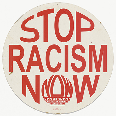 circular cardboard placard with red text reading "Stop Racism NOW," with the "O" in "NOW" formed from the acronym of the National Organization for Women